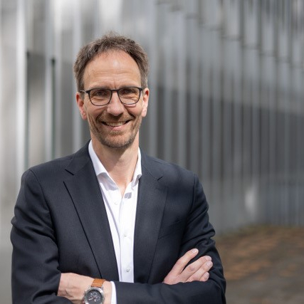 Ein Portrait von Prof. Dr. Thomas Abel. Er steht lächelnd vor einem Gebäude und hat die Arme locker vor dem Oberkörper verschränkt