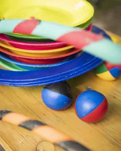 Auf einem Biertisch liegen verschiedene bunte Spielzeuge, zum Beispiel Jonglierbälle, Hulahoop-Reifen, Ringe und Balancierteller.