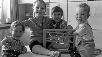 Vier Kinder mit Köperbehinderungen sitzen auf einem Tisch und spielen mit einer Murmelbahn. Sie lachen.