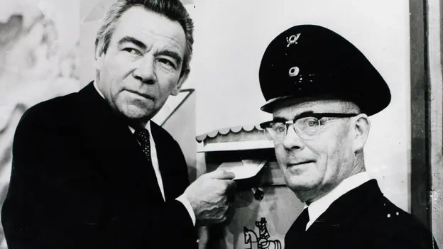 Peter Frankenfeld und ein Postbeamter stehen vor reinem Briefkasten und werfen einen Brief ein.