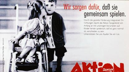 Ein Mädchen im Rollstuhl küsst einen Jungen neben ihr auf die Wange. Rechts steht der Schriftzug "Wir sorgen dafür, dass sie gemeinsam spielen".