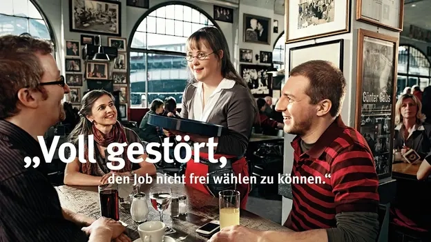 Eine junge Frau mit Down-Syndrom nimmt in einem Restaurant die Bestellung von drei Gästen auf.