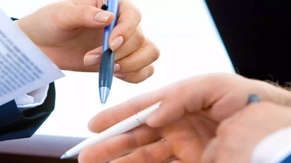 Die Hände von zwei Personen halten Stifte und Unterlagen.