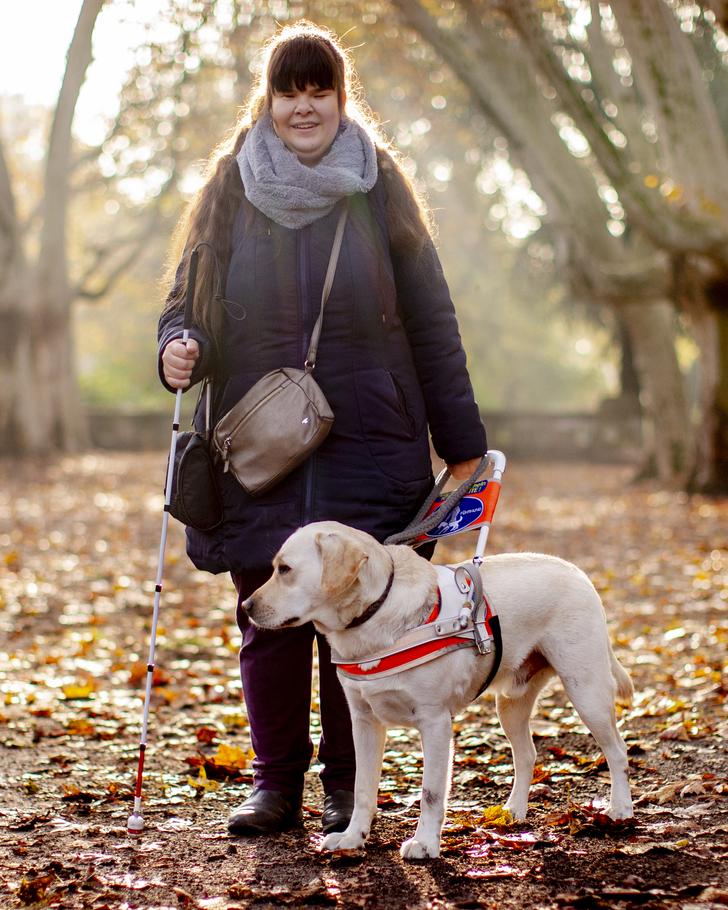 Eine Frau steht mit ihrem Blindenhund auf einem Fußweg.