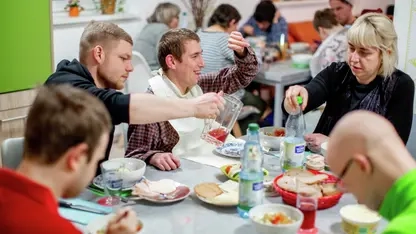 Frauen und Männern  mit und ohne Behinderung sitzen beim gemeinsamen Essen am Tisch.