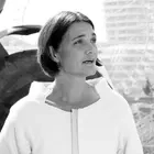 Schwarz-weiß Bild einer Frau im Rollstuhl auf einer Baustelle. Sie hält einen Gebäudeplan und einen Stift in der Hand.