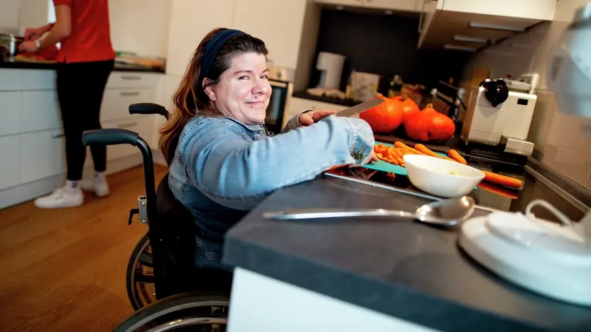Eine Frau im Rollstuhl schneidet auf einer unterfahrbaren Küchenarbeitsplatte Gemüse.