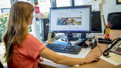 Eine Frau sitzt vor dem Computer. Auf dem Bildschirm ist die Starteseite des Aktion Mensch-Familienratgebers zu sehen.