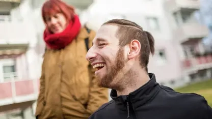 Ein lächelnder junger Mann und eine Frau vor einem Wohngebäude