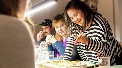 Vier Personen mit und ohne Behinderung sitzen gemeinsam bei einer Mahlzeit am Tisch.