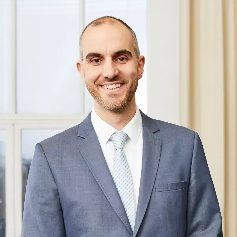 Ein junger Mann in grau-blauem Anzug lächelt in die Kamera.