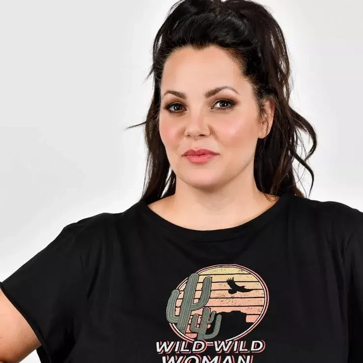Eine junge Frau hat ihre dunklen Haare zu einem Zopf zusammengebunden. Sie schaut herausfordernd in die Kamera. Auf ihren schwarzen T-Shirt steht der Text "Wild Wild Woman".