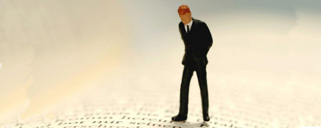 Kleines Figürchen eines Mannes steht auf den Seiten eines Buches und betrachtet die Buchstaben