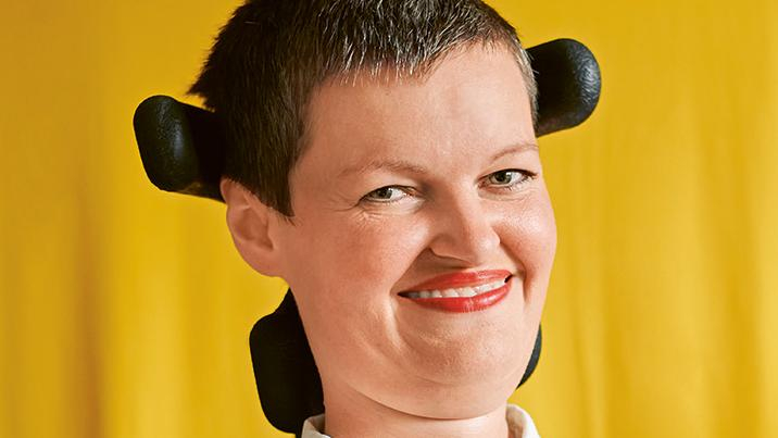 Eine Frau mit kurzen Haaren im Rollstuhl lächelt