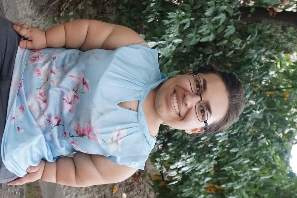 Porträt einer jungen, kleinwüchsigen Frau vor einer Hecke 