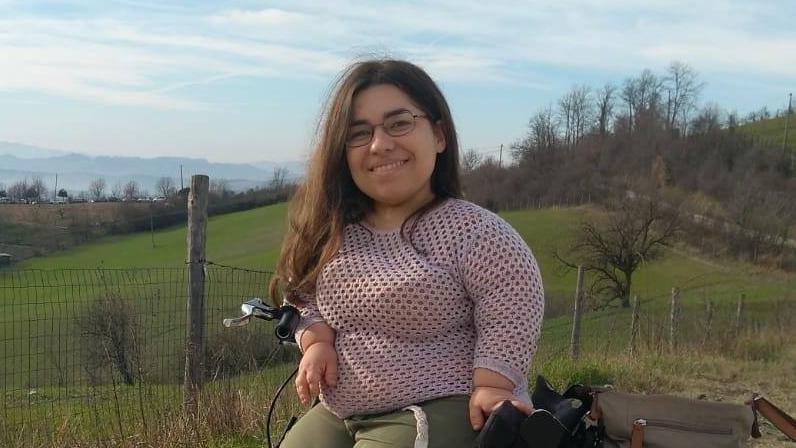 Eine junge, kleinwüchsige Frau mit Laufrad auf einer Wiese 