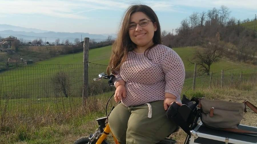 Eine junge, kleinwüchsige Frau mit Laufrad auf einer Wiese 