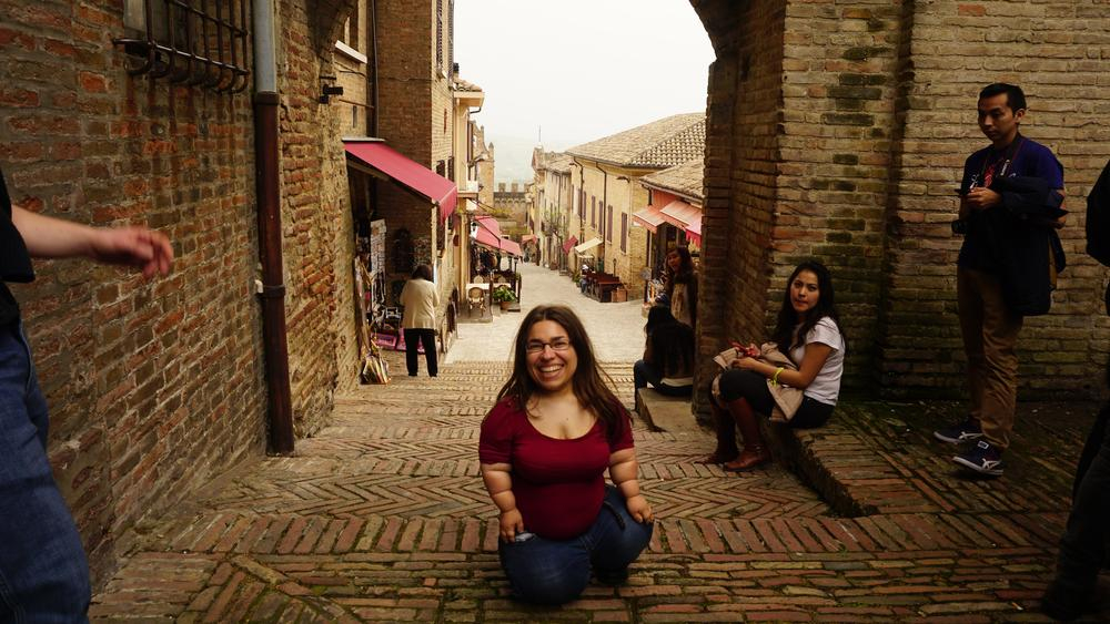 Eine junge, kleinwüchsige, lachende Frau in einer italienischen Gasse 