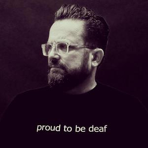 Mann mit Brille und Bart. Auf seinem Oberteil steht: stolz gehörlos zu sein