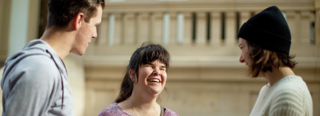 Carina unterhält sich in der Uni mit zwei Studenten und lacht.