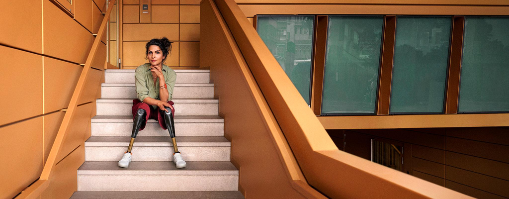 Eine Frau sitzt auf einer Treppe. Sie trägt zwei Beinprothesen und schaut auffordernd in die Kamera.