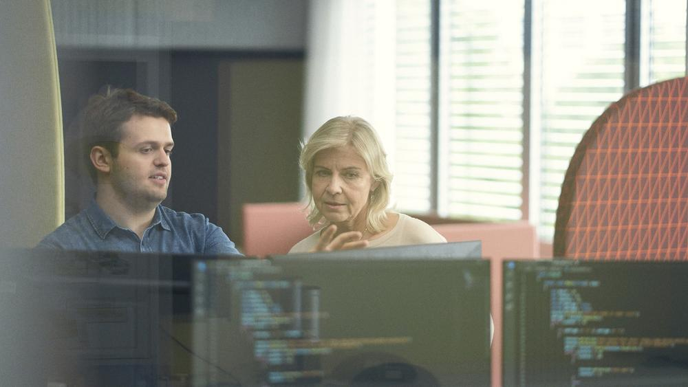 Ein junger Mann und eine blonde Frau sitzen gemeinsam vor einem Computerbildschirm und arbeiten.
