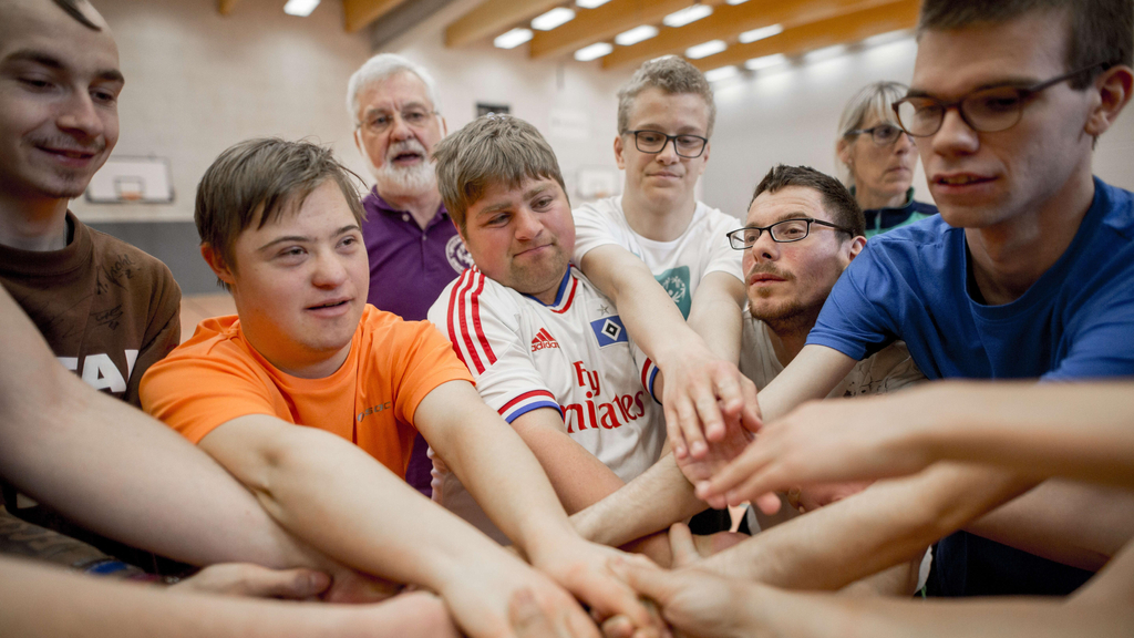 Ein Gruppe von Menschen mit und ohne Behinderung fassen sich gemeinsam an den Händen.