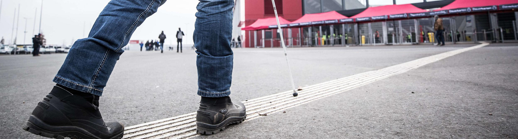 Eine Person mit Langstock folgt den Leitlinien auf dem Boden zum Fußballstadion des FSV Mainz.