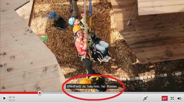 Das Bild von einem Video von zwei Kletterern in einem Klettergarten. Am unteren Bildrand sind Untertitel eingeblendet, die rot umkringelt sind.