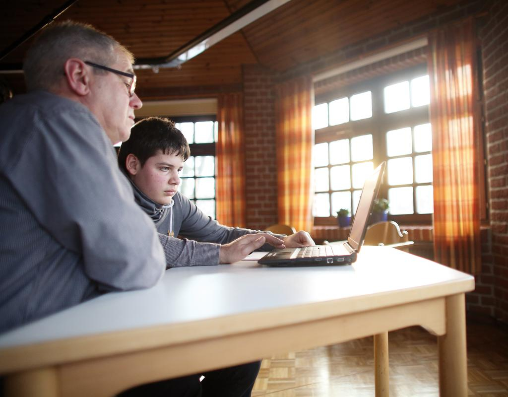 Ein Junge und ein Herr sitzen gemeinsam an einem Tisch und schauen auf einen Laptop.