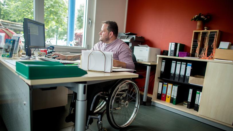 Ein Mann im Rollstuhl sitzt an seinem Schreibtisch vor dem Rechner.