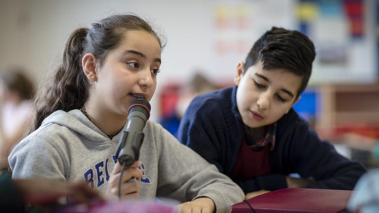 Ein Mädchen in einer Schulklasse spricht ins Mikrofon. 