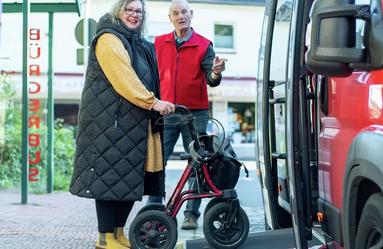 Eine Frau mit Rollator geht über eine Rampe in einen Bus