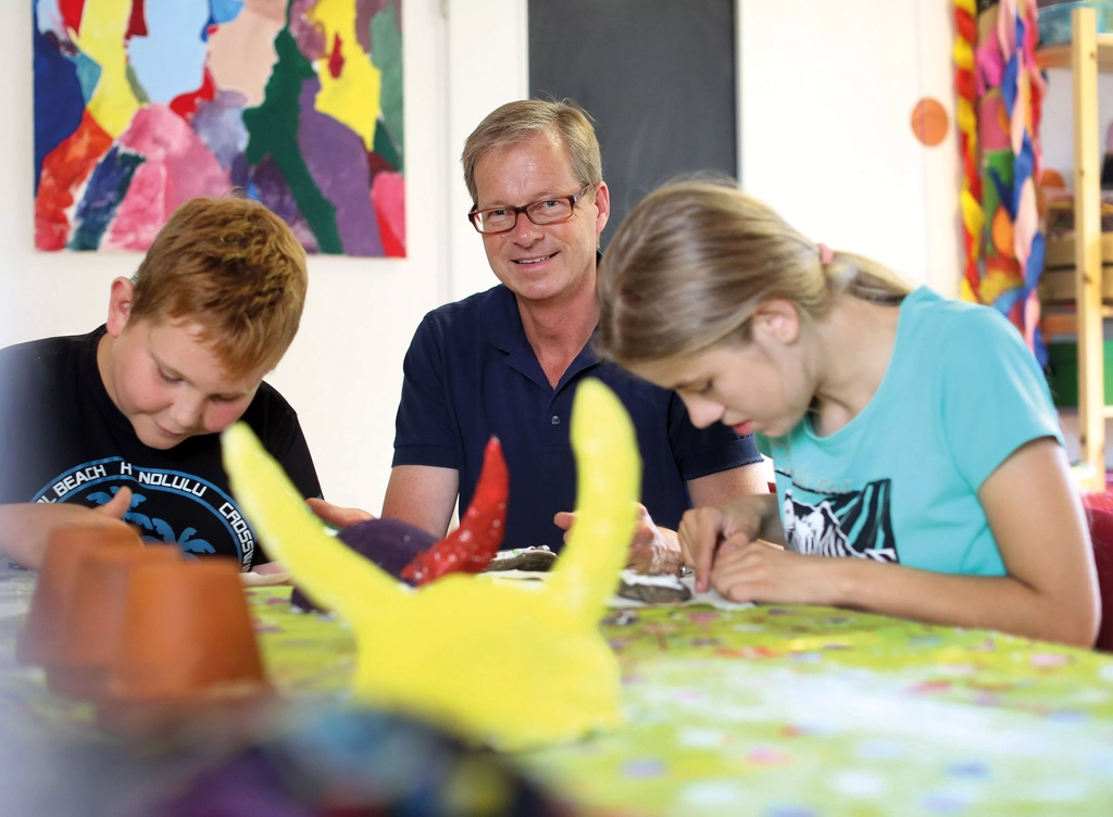 Armin von Buttlar sitzt am Tisch mit bastelnden Kindern. 