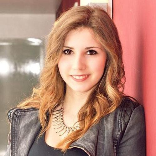 Fotoporträt einer jungen Frau mit langen, hellbraunen Haaren und dunklen Augen, sie lächelt in die Kamera