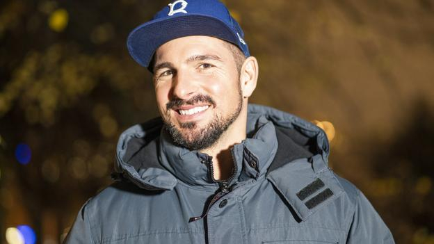 Benjamin Piwko: Porträtfoto eines junger Manns mit Bart und Basecap abends draußen.