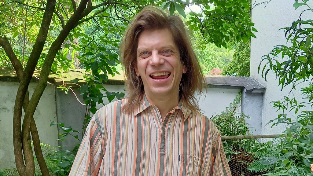 Ein lachender Mann mittleren Alters steht in einem Garten 