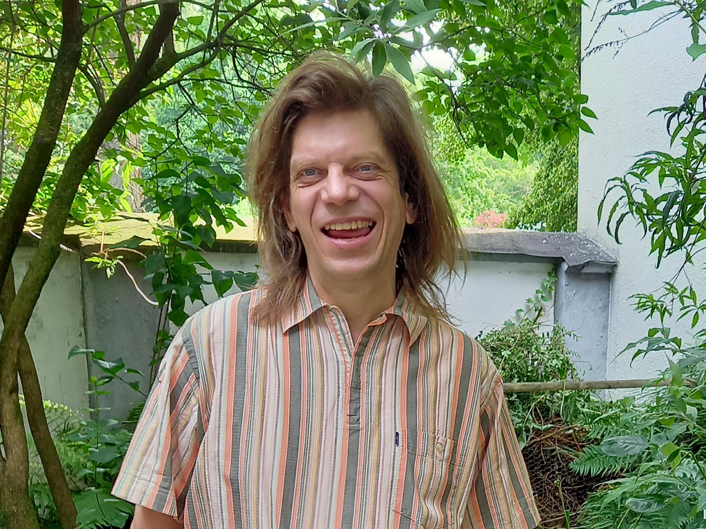 Ein lachender Mann mittleren Alters steht in einem Garten 