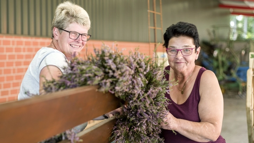 Zwei Frauen binden Blumen an einen Wagen und lächeln.