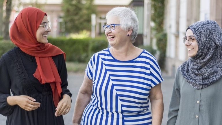 Drei Frauen lachen miteinander, eine ist etwas älter, zwei tragen ein Kopftuch