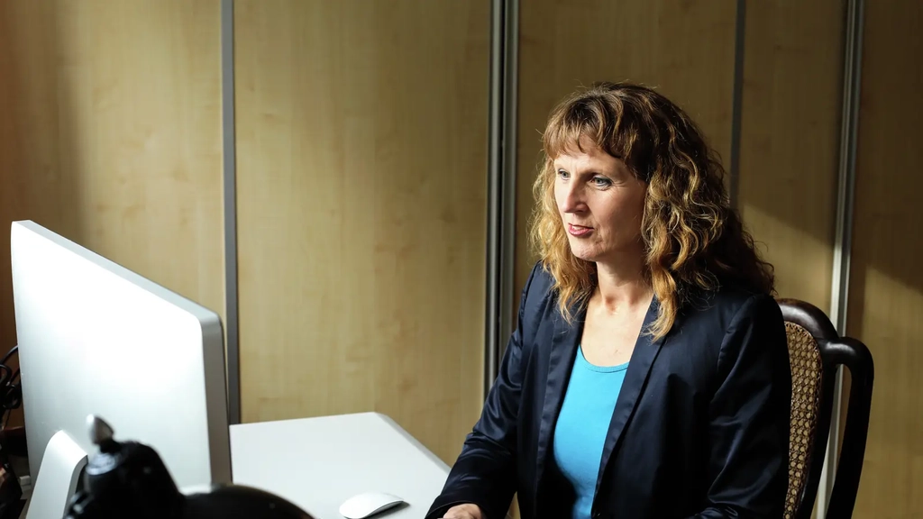 Eine Frau mit langen gelockten Haaren sitzt vor einem Computer. Sie schaut auf den Bildschirm und hat ihre Hände auf der Tastatur liegen.