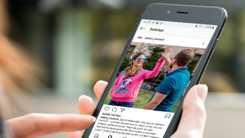 Eine Frau hält ein Smartphone in der Hand, auf dem der Instagram-Account der Aktion Mensch aufgerufen ist.