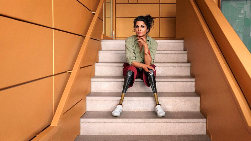 Eine Frau sitzt auf einer Treppe. Sie trägt zwei Beinprothesen und schaut auffordernd in die Kamera.