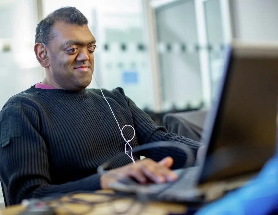 Ein Mann sitzt an einem Laptop und hat einen Kopfhörer im Ohr.
