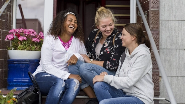 Drei junge Frauen sitzen auf einer Eingangstreppe und lachen.