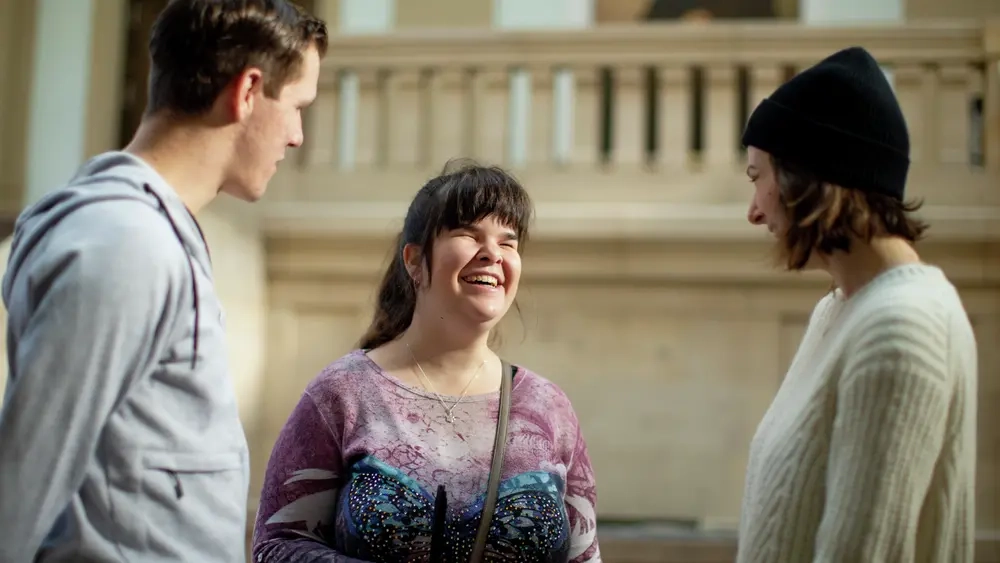 Carina unterhält sich in der Uni mit zwei Studenten und lacht.