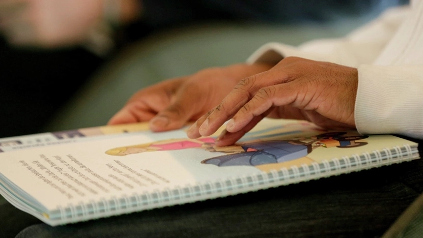 Ein aufgeschlagenes Buch, das eine Person in Brailleschrift liest. Es sind nur die Hände der Person und das Buch zu sehen.