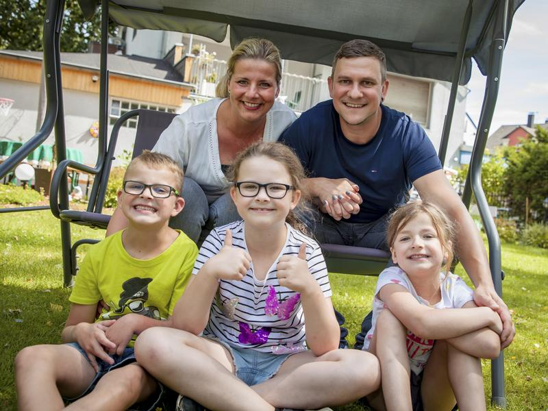 Familie Buhrmeister in ihrem Garten. Die Eltern sitzen auf einer Hollywoodschaukel, die Kinder davor. Alle lachen.