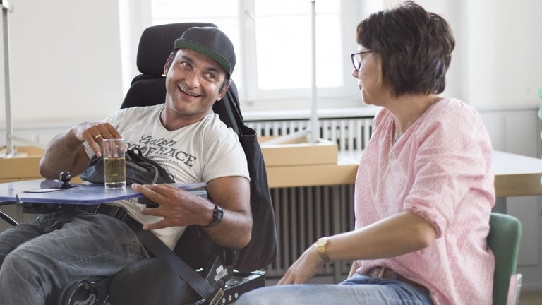 Ein junger Mann im Rollstuhl schaut seine Sitznachbarin