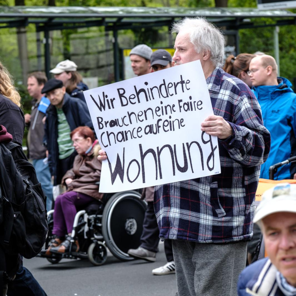 Ein Demonstrant auf der Straße hält ein Schild mit der Vorderung nach mehr behindertengerechten Wohnungen